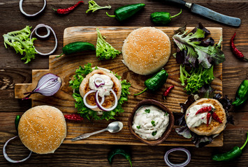 Chicken burgers with fresh salad, onion, peppers and mayonnaise sauce. Overhead view and dark,...