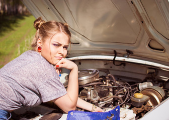 Beautiful young woman repairing an old car. The woman is upset because she does not know how to fix...