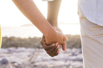 closeup of two lover hands stay together with a sunset backlight in background faraway. love and...
