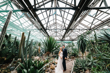 The groom in wedding suit and the bride in dress are standing in the Botanical green garden full of...