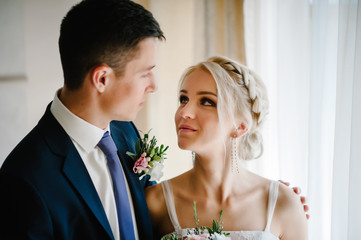 Portrait of the bride and groom near the window indoors in the rooms. Man and woman.