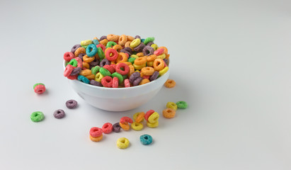 Messy bowl of sugar coated fruity flavored cereal with milk on a white counter top.