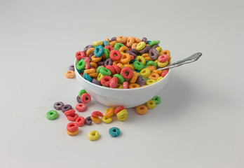 Messy sugar coated fruity flavored cereal in a bowl with milk and spoon in the food atop a white counter top.