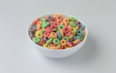 Dry sugar coated fruity flavored cereal in a bowl atop a white counter top.