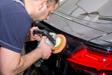 A man polishes a black car with a polisher