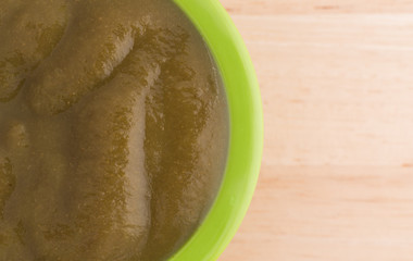 Top close view of a bowl of organic spinach baby food on a table.