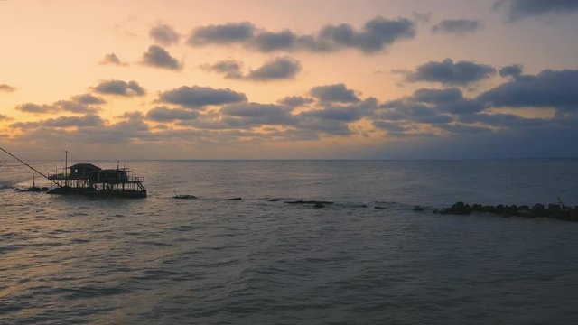 Vista aerea di sagome dei trabucchi sul mare per la pesca del pesce con pescatori alle ultime luci del tramonto.
