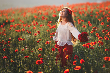 Naklejka na ściany i meble Young beautiful woman walking and dancing through a poppy field at sunset