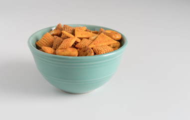 Snack crackers and pretzels in a small bowl atop a white counter top.