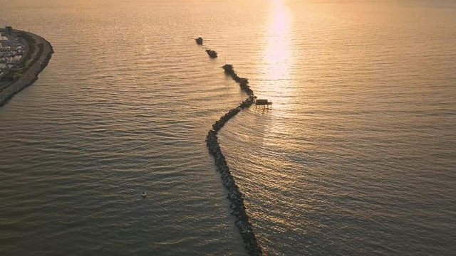 Vista aerea di sagome dei trabucchi sul mare per la pesca del pesce con pescatori alle ultime luci del tramonto.