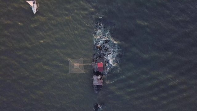 Vista aerea di sagome dei trabucchi sul mare per la pesca del pesce con pescatori alle ultime luci del tramonto.