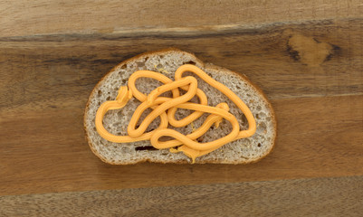 Top view of canned cheese on a slice of wheat bread on a wood cutting board.