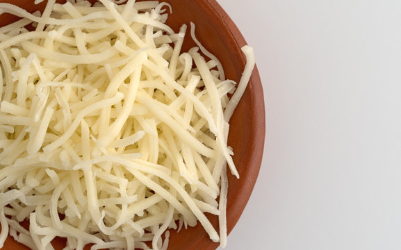 Top close view of sharp white cheddar cheese in a small bowl on a counter top.