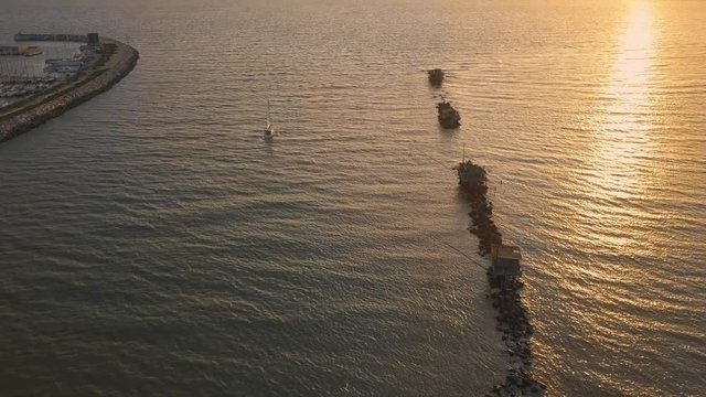 Vista aerea di sagome dei trabucchi sul mare per la pesca del pesce con pescatori alle ultime luci del tramonto.