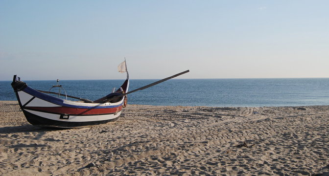 Barco a olhar para o horizonte, barco de pesca em costa portuguesa parado na areia da praia ao por do sol