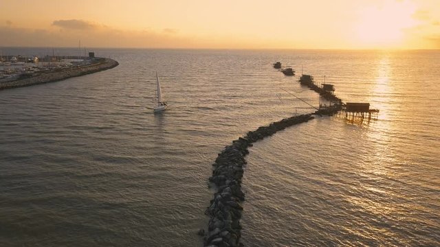 Vista aerea di sagome dei trabucchi sul mare per la pesca del pesce con pescatori alle ultime luci del tramonto.