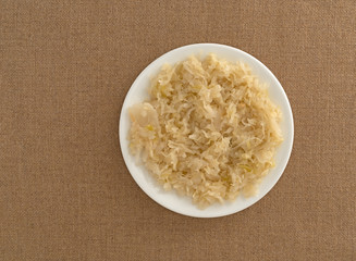 Top view of sauerkraut on a white plate atop a tablecloth.