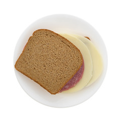 Top view of a Genoa salami and provolone cheese wheat bread sandwich on a plate isolated on a white background.