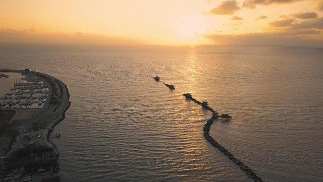 Vista aerea di sagome dei trabucchi sul mare per la pesca del pesce con pescatori alle ultime luci del tramonto.