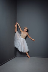 Fototapeta na wymiar Patient flexible ballerina standing near the wall and stretching.