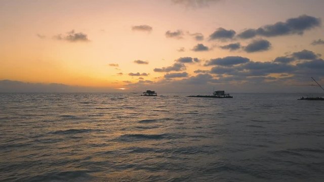 Vista aerea di sagome dei trabucchi sul mare per la pesca del pesce con pescatori alle ultime luci del tramonto.