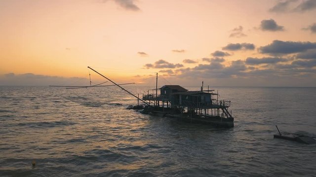 Vista aerea di sagome dei trabucchi sul mare per la pesca del pesce con pescatori alle ultime luci del tramonto.