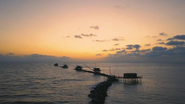 Vista aerea di sagome dei trabucchi sul mare per la pesca del pesce con pescatori alle ultime luci del tramonto.