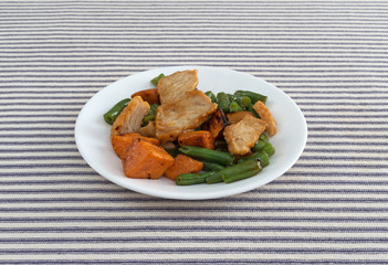 Side view of a roasted turkey TV dinner on a plate atop a blue striped tablecloth.