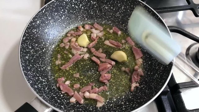 Time lapse of cooking slices of bacon and garlic in olive oil.