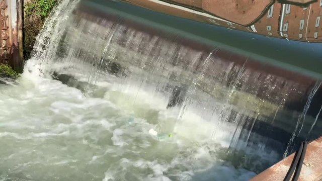 Plastic pollution in a limpid waterfall with many foam in a lock in a sunny day.