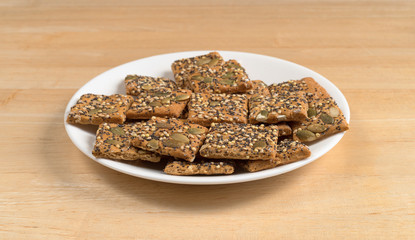 Several whole wheat seeded crackers on a white plate atop a wood table.