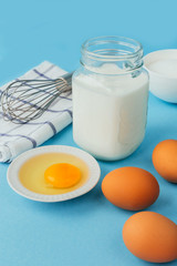 Obraz na płótnie Canvas Eggs of chicken, flour in a bowl, sugar, milk in a glass jar whisk ingredient for cooking a bake on a blue background with copy space
