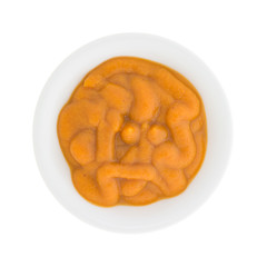 Top view of a bowl of organic pumpkin and carrot baby food isolated on a white background.