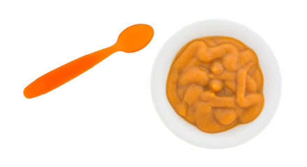 Bowl of organic pumpkin and carrot baby food with an orange plastic spoon to the side.