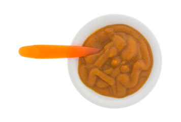 Top view of a bowl of organic pumpkin and carrot baby food with a spoon in the food isolated on a white background.