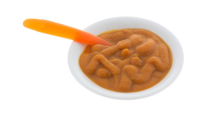 Bowl of organic pumpkin and carrot baby food with a spoon in the food isolated on a white background.