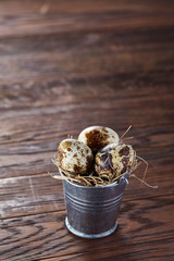 Small decorative bucket filled with quail eggs dark wooden table, close-up, selective focus.
