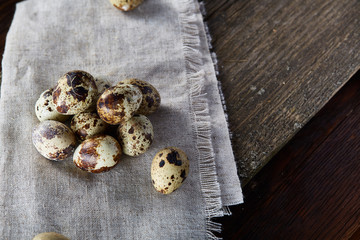 Quail eggs arranged in pyramid on a napkin with boxwood branches over a wooden table, close-up, selective focus.