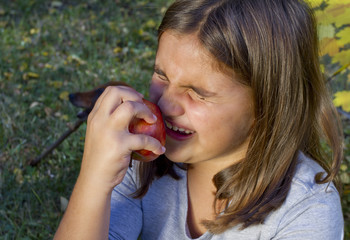 Child bite a red apple and has a heavy toothache.  Cute little girl eat orange fruit apple and feel tooth pain.  Closeup portrait of kid cries of tooth pain. Little kid with sensitive toothache cries.
