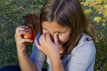 Child bite a red apple and has a heavy toothache.  Cute little girl eat orange fruit apple and feel tooth pain.  Closeup portrait of kid cries of tooth pain. Little kid with sensitive toothache cries.