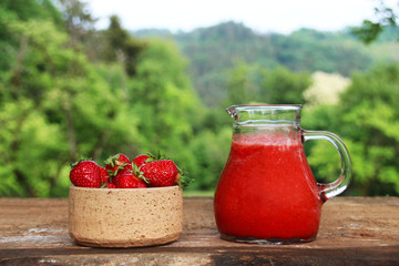 A bowl and glass kettle of strawberries on a wooden table