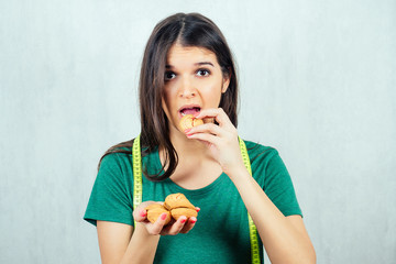 Fototapeta premium portrait of a hungry, young and beautiful woman holding a cookie in a T-shirt and measuring tape. concept of diet and rejection of unhealthy harmful food