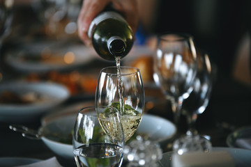 Pouring white wine from bottle into the wine glass.