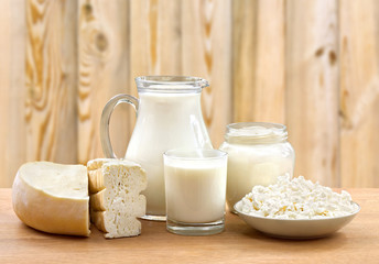 Milk, sour cream, cheese and cottage cheese on wooden table on wooden background with space for text