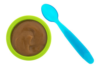 Top view of pears and blackberry organic baby food in a green bowl with a blue plastic spoon to the side isolated on a white background.