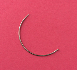 Curved upholstery cloth needle on a red paper background.