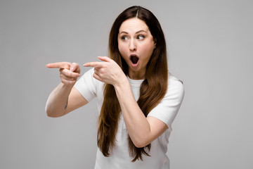Fototapeta premium Portrait of emotional astonished plus size model standing in studio looking in camera showing on blank area