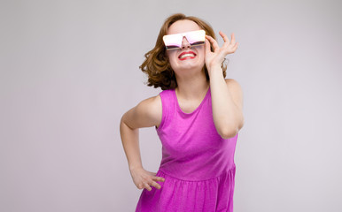 Charming young girl in pink dress on gray background. Cheerful girl in square glasses. The girl...