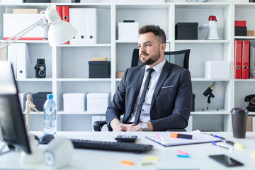 A man is sitting in a chair in the office at the table.