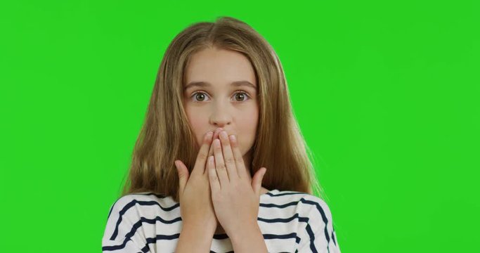Close up of the blonde teenager girl with long hair in the striped blouse closing her mouth with hands and doing oops grimacing face. Green screen. Chroma key